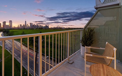 A balcony with a chair and table overlooking a city skyline at dusk.