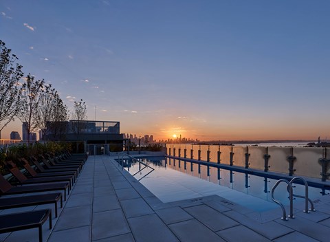 A sunset view of a pool area with lounge chairs and a railing.
