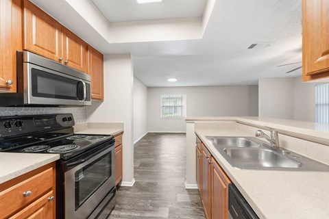 A kitchen with a black stove top oven and microwave, wooden cabinets, and a sink.