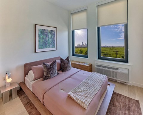 A bedroom with a large bed and a window with a view of a city skyline.