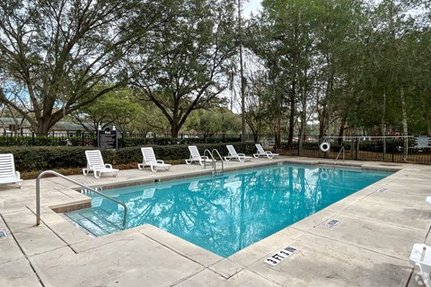 A pool surrounded by trees and lounge chairs.