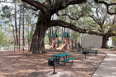 A playground with a green slide and picnic tables.