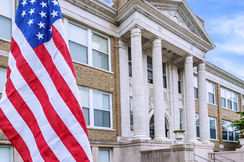 An American flag hangs in front of a building with columns.