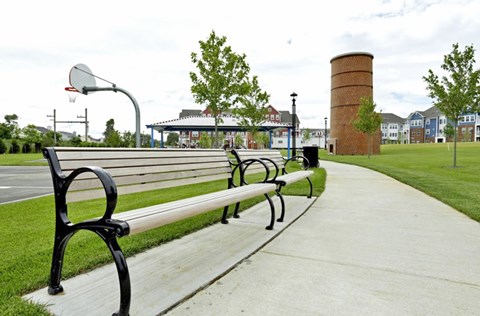 A park bench is on a sidewalk next to a basketball hoop.