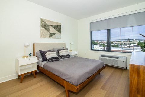 A bedroom with a bed, nightstand, and window overlooking a cityscape.