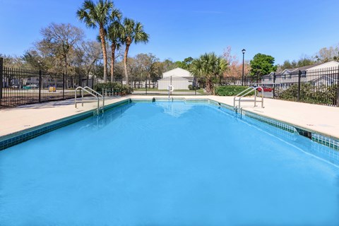 A swimming pool surrounded by a black fence with trees in the background.