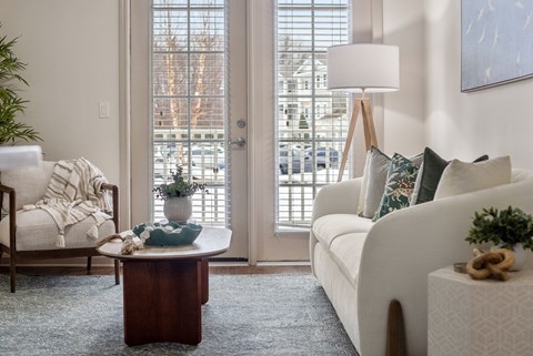 A living room with a white couch, a wooden table, and a chair with a white blanket.