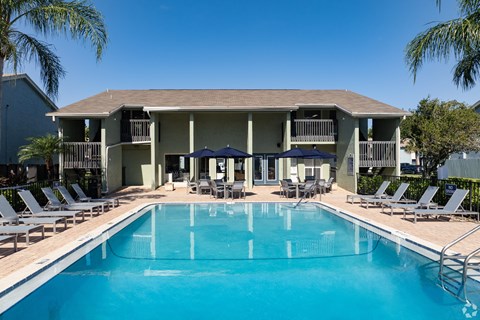 A large swimming pool in front of a building with lounge chairs and umbrellas.