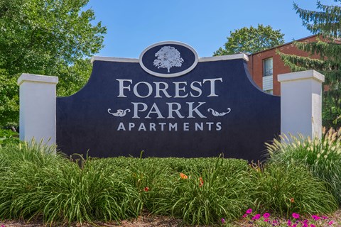 A sign for Forest Park Apartments is surrounded by green plants and flowers.