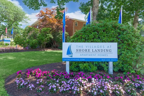 A sign for The Villages at Shore Landing Apartment Homes is in front of a building and trees.