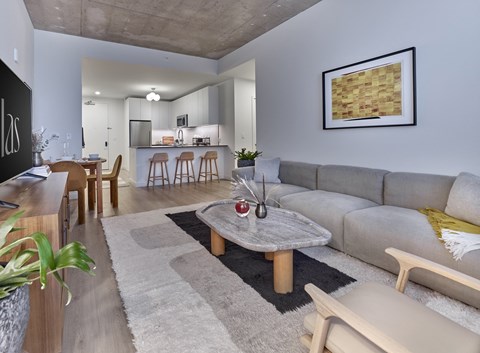 A modern living room with a grey sofa, wooden coffee table, and a large painting on the wall.