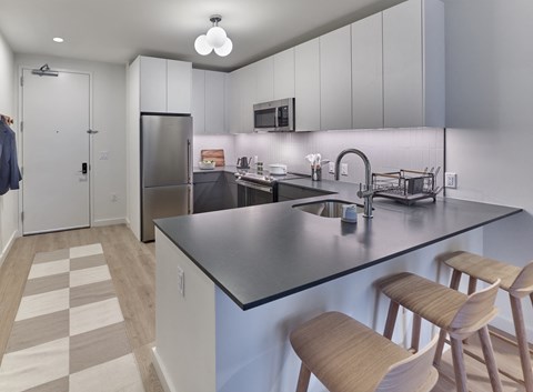 A kitchen with a black counter top and wooden bar stools.