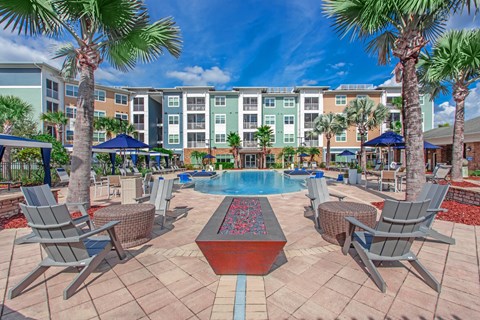 A pool surrounded by chairs and umbrellas with apartment buildings in the background.