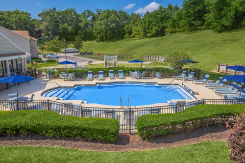 A large outdoor swimming pool surrounded by a metal fence and lounge chairs.