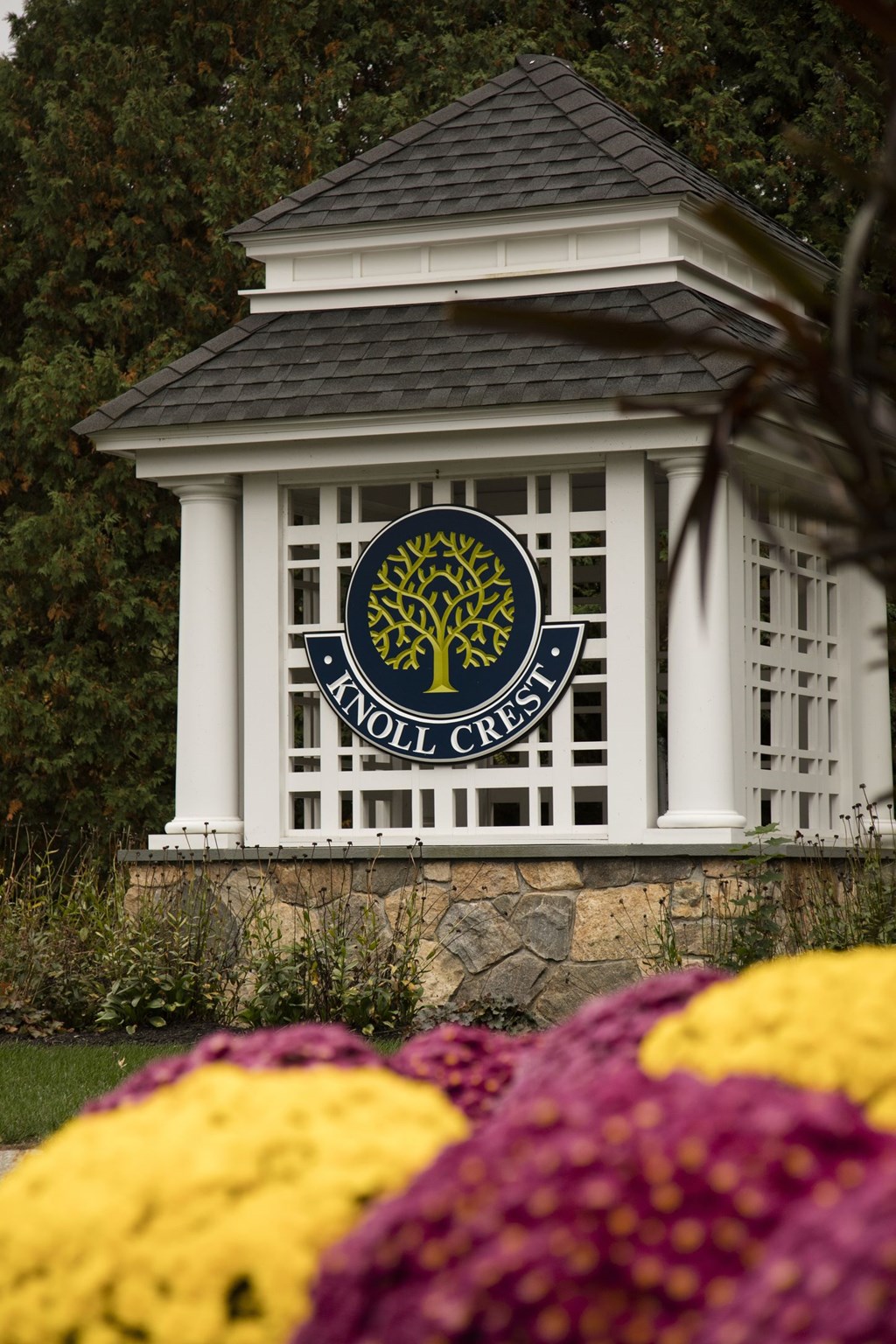 A white gazebo with a tree logo on the front and a stone wall below it.