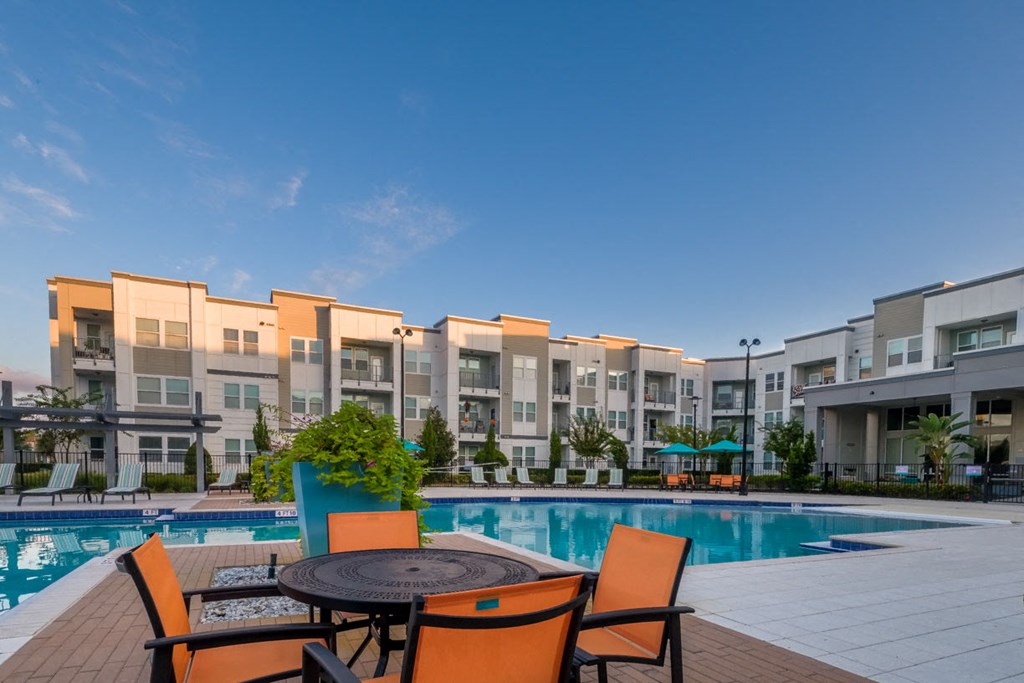 a swimming pool at an apartment complex with orange chairs and a table at Linden on the GreeneWay, Orlando, 32824