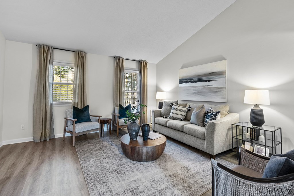 A living room with a grey couch, a coffee table, and a large painting on the wall at West Oak Apartments, Wake Forest