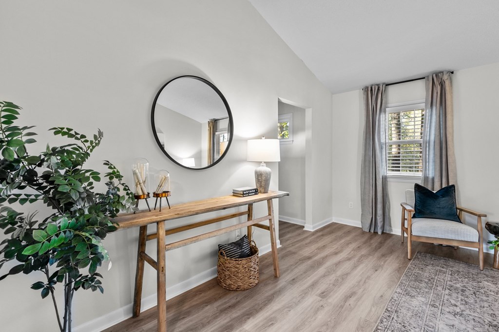 A room with a round mirror, a wooden table, a chair, and a potted plant at West Oak Apartments, Wake Forest, 27587