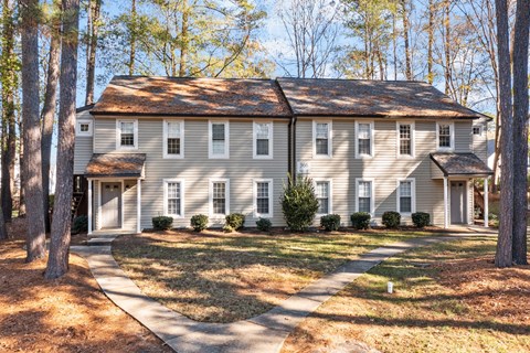 A large house with a grey roof and white walls is surrounded by trees at West Oak Apartments, Wake Forest, 27587