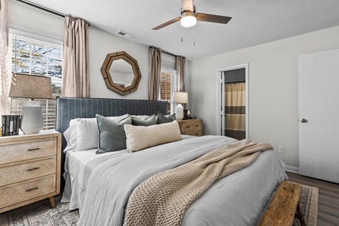 A bedroom with a large bed, a ceiling fan, and a mirror on the wall at West Oak Apartments, Wake Forest, NC 27587