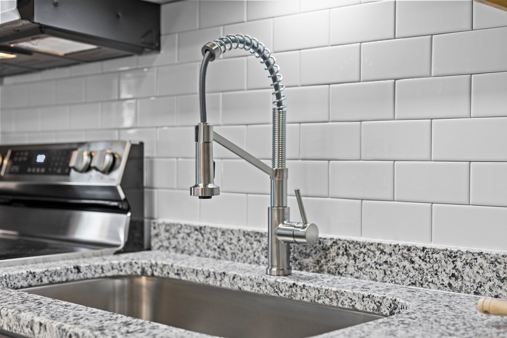 A kitchen sink with a chrome faucet and a tile backsplash at West Oak Apartments, Wake Forest, 27587