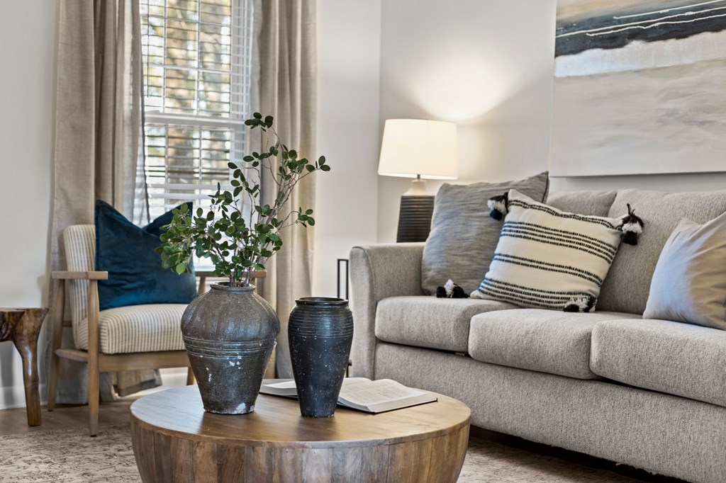 A living room with a grey couch, a wooden table, and a painting on the wall at West Oak Apartments, North Carolina