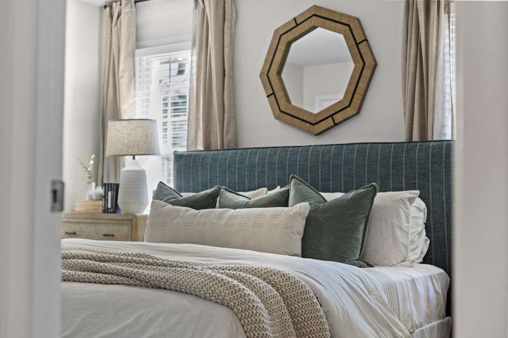 A bedroom with a bed, pillows, a mirror, and a lamp at West Oak Apartments, North Carolina 27587