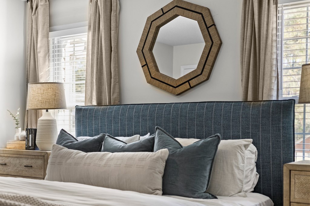 A bedroom with a bed, pillows, a mirror, and lamps at West Oak Apartments, Wake Forest, 27587