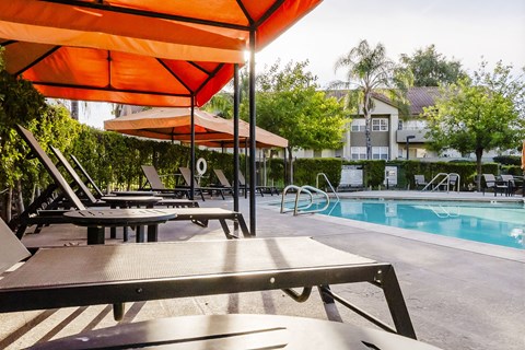 A poolside area with sun loungers and an orange umbrella. at Legends at Rancho Belago, Moreno Valley