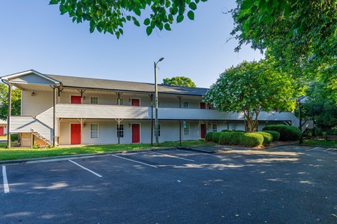 an empty parking lot in front of a white building with red doors at Ashford Place Apartments, Kannapolis, NC