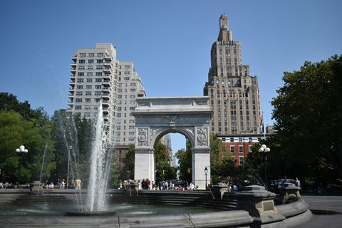 A fountain in front of a large archway and buildings.