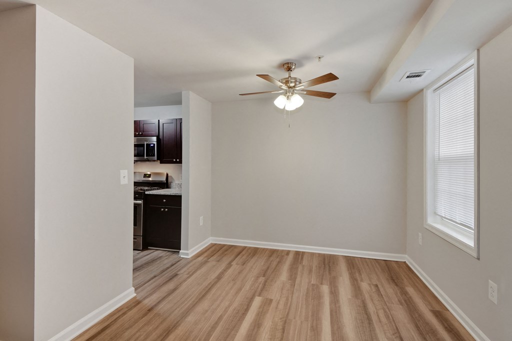 an empty living room with a ceiling fan and a kitchen