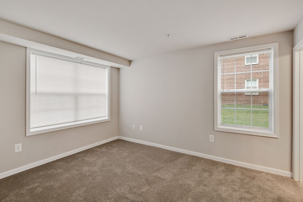 an empty living room with two windows and carpeting
