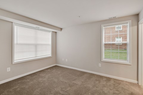 an empty living room with two windows and carpeting