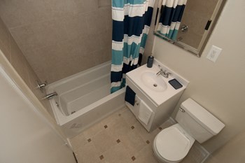 Bathroom with white sink, toilet and a blue striped shower curtain at Laurel Pines Apartments in Laurel, MD Bathroom with blue striped shower curtain - Photo Gallery 4