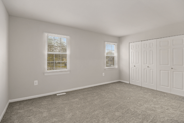 an empty bedroom with two windows and white doors