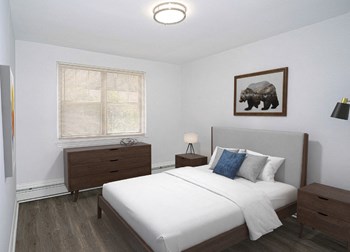 Bedroom at Drumcastle Apartments A bedroom with white walls and gray-brown vinyl floors. There is a full-size bed with a gray headboard and white comforter. A bear painting hangs on the wall above the headboard. There are wooden end tables on both sides of the bed and a dresser against the wall to the left under a window - Photo Gallery 4