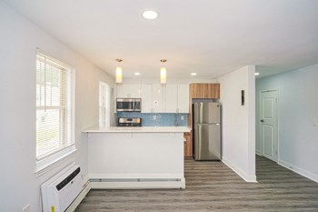Living Room and Kitchen at Drumcastle Apartments kitchen with blue tile backsplash, white cabinets, and stainless-steel fridge, microwave, and oven. The walls are painted white and the floor is gray-brown vinyl. - Photo Gallery 5