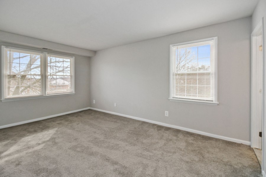an empty bedroom with two windows and a carpeted floor