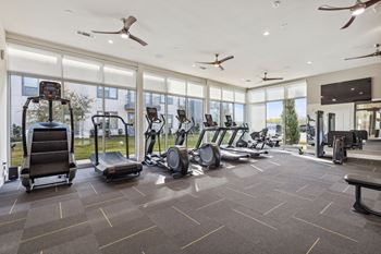 the state of the art gym is equipped with cardio equipment and floor to ceiling windows at LynnCora in Grand Prairie, TX