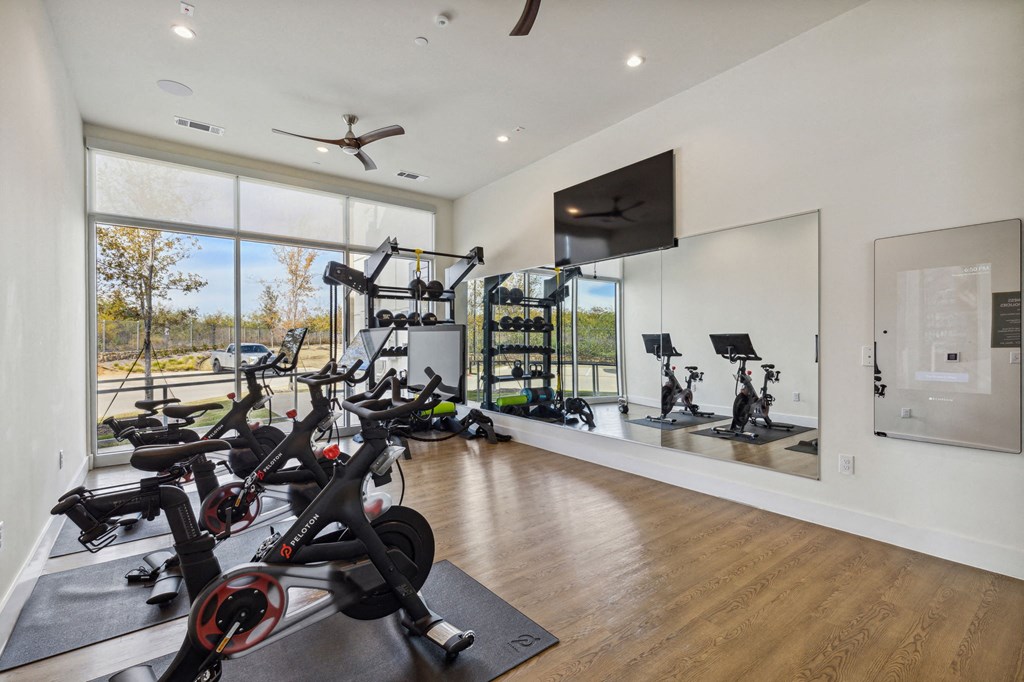 a home gym with various exercise bikes and a television on the wall at LynnCora, Grand Prairie, Texas