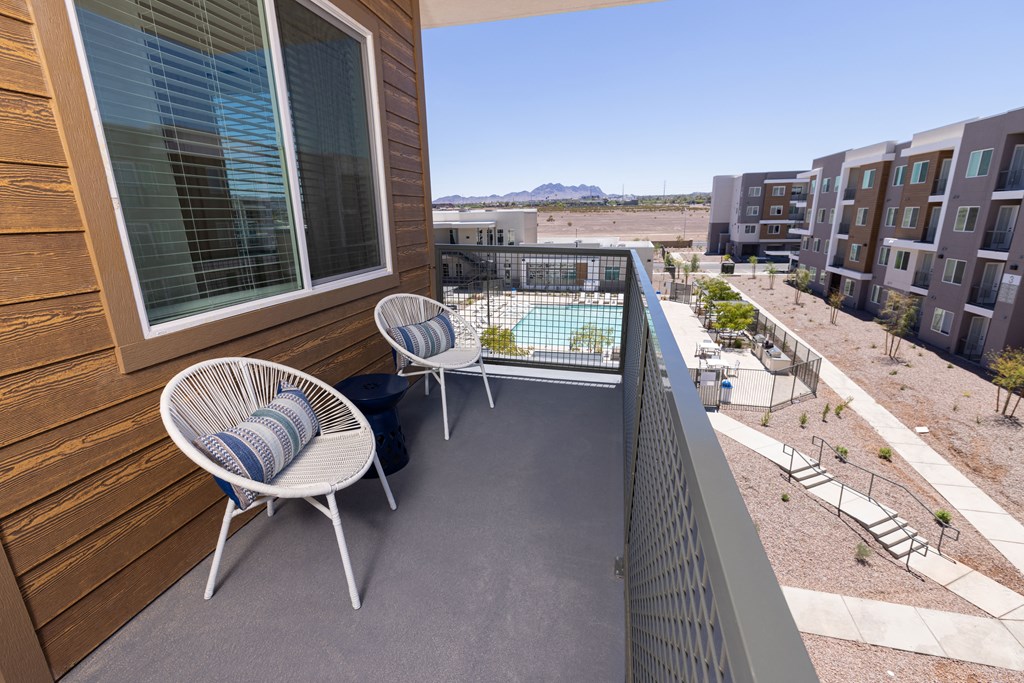 a balcony with two chairs and a table and a pool in the background