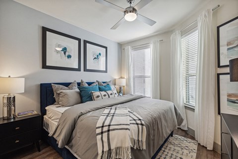 Bedroom with navy upholstered bed and ceiling fan at LynnCora Apartments, Grand Prairie, TX