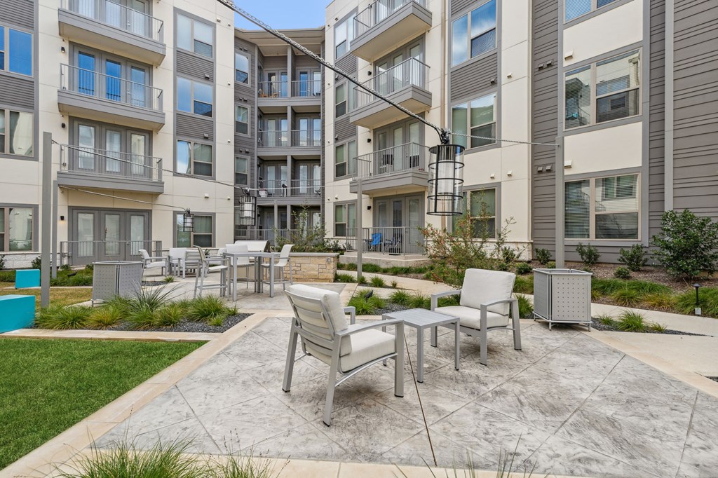 an outdoor patio courtyard with tables and chairs in front of an apartment building at LynnCora, Grand Prairie