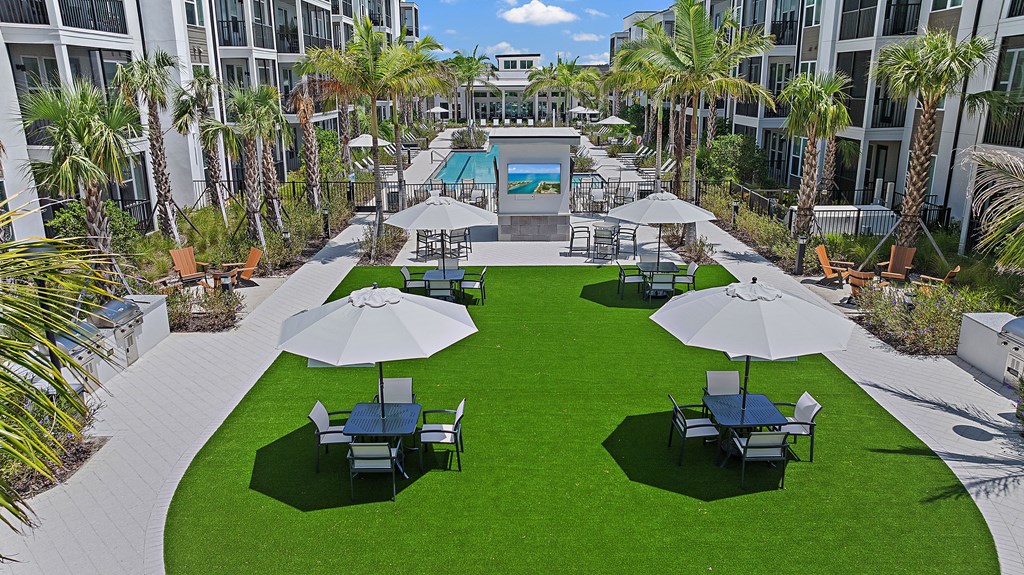 A large grassy area with a pool and umbrella tables. at Mira at Palmer Ranch, Florida