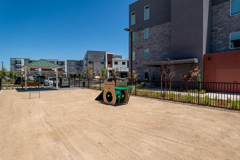 A green and yellow wheelbarrow is in the foreground of a dirt parking lot.