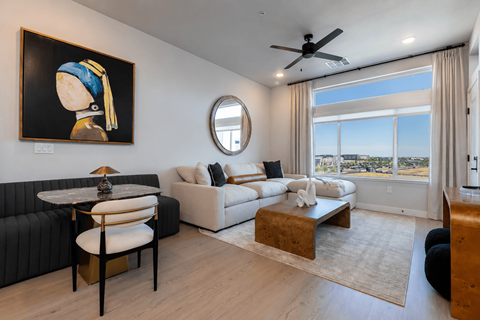 A living room with a painting of a woman, a black sofa, a white couch, a coffee table, and a view of the city.