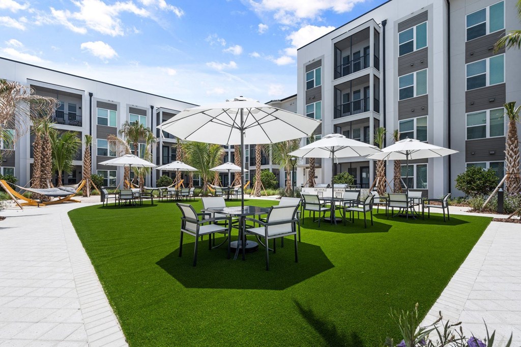a courtyard with tables and umbrellas in front of a Mira at Palmer Ranch apartment building