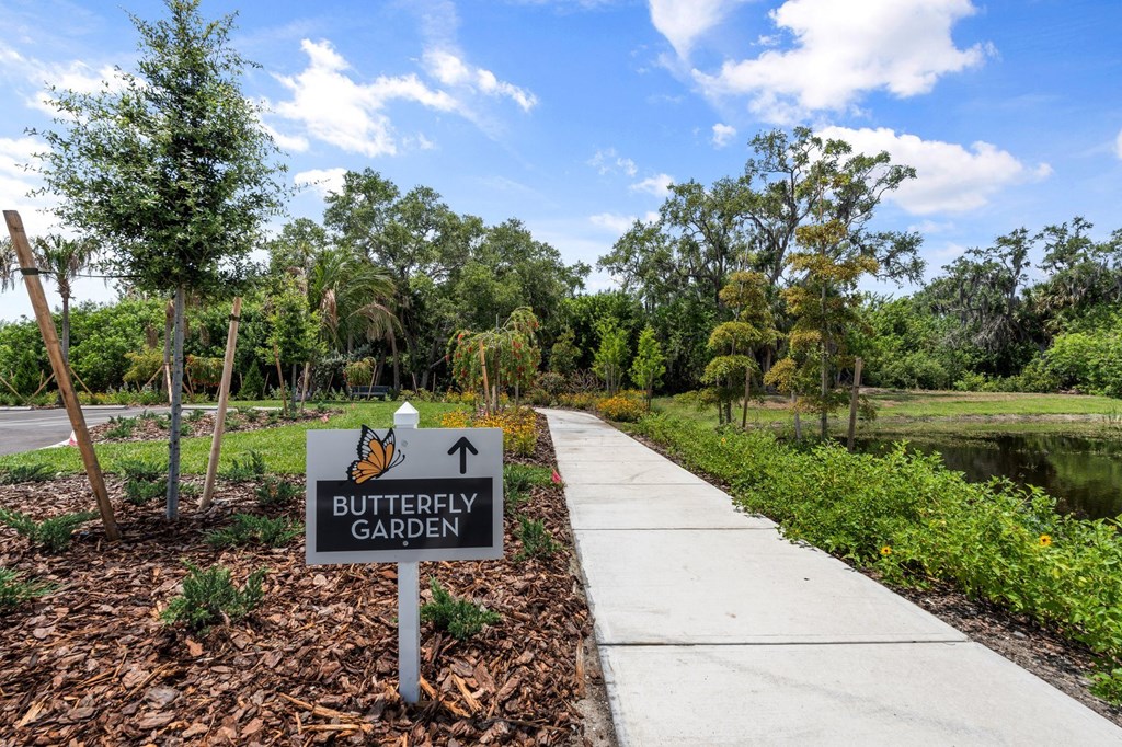 a sign for the butterfly garden next to a sidewalk
