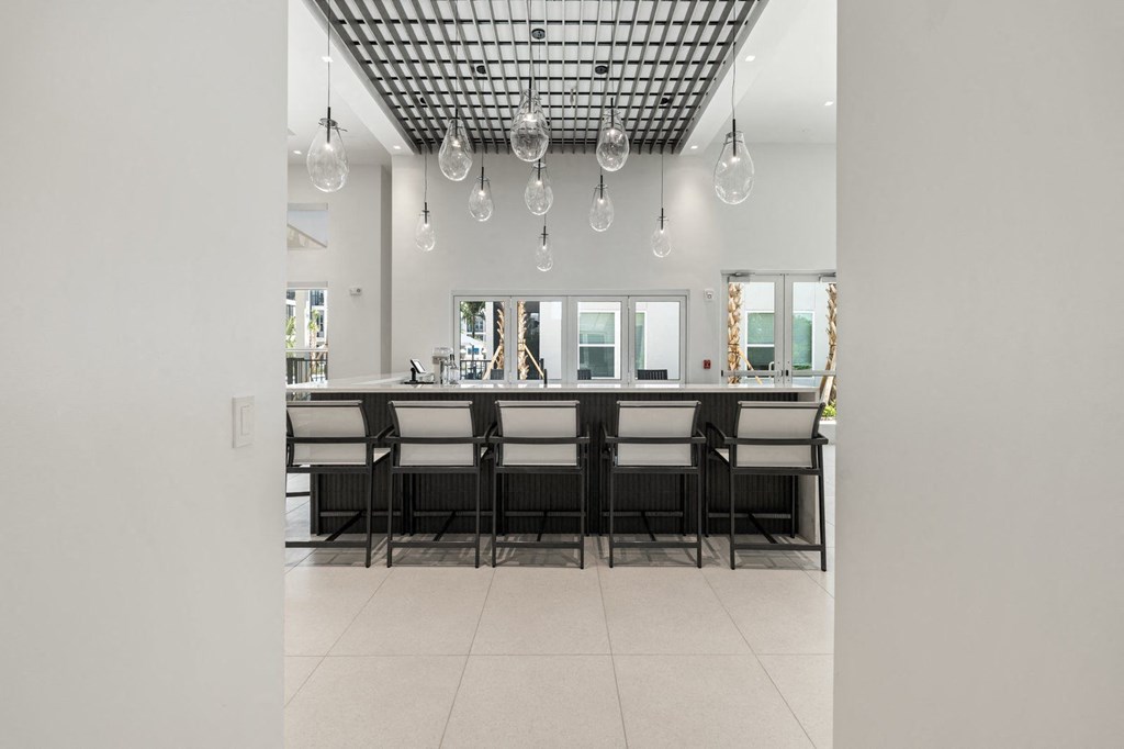 the kitchen has a large island with chairs and a row of hanging lights